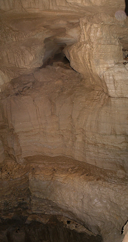 Photo looking across a large cave shaft, showing a tall vertical
							rock face with a tunnel entrance near the top