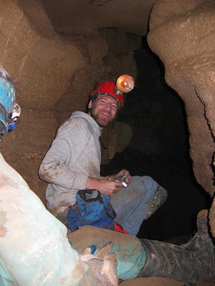 Photo of the author crouching next to the entrance to a cave
							passage