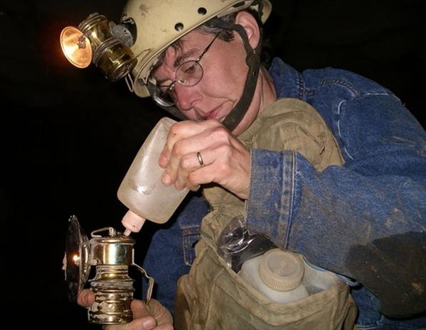 Photo of a caver refilling a lamp from a small bottle