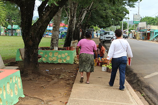 Picture of two people walking down a sidewalk with trees on the left side