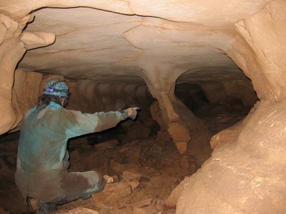 Photo of a caver pointing into a large tunnel
