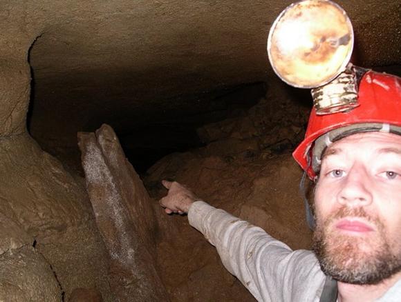 Photo of the author pointing into a dark cave passage